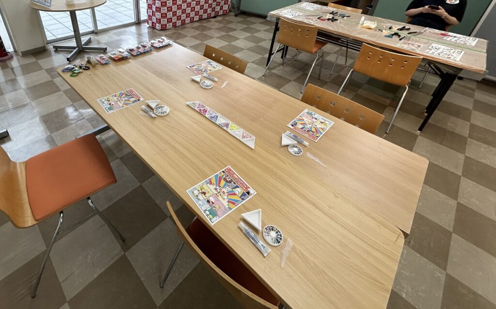 住宅展示場のイベント会場に用意された、南京錠デコとオリジナル転写ポーチ制作ワークショップの準備風景。必要な道具が整然と並べられたテーブル。