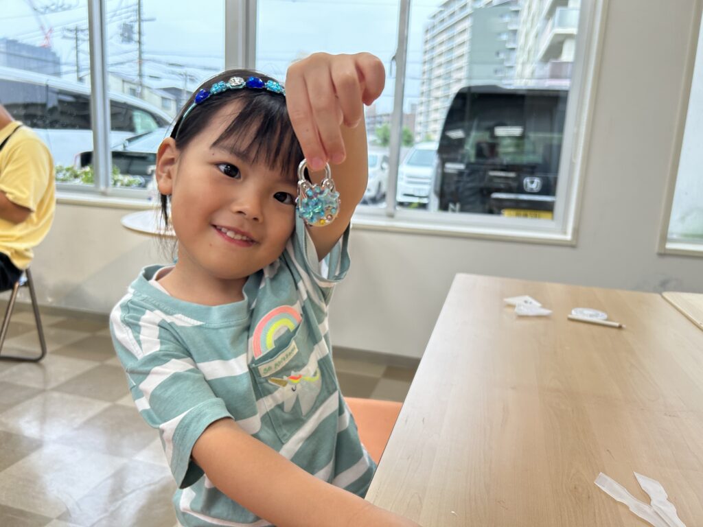 完成したキラキラのデコ南京錠を掲げて微笑むお子様。自分の手で作った「世界に一つだけの作品」に満足し、住宅展示場での体験が楽しい思い出となった瞬間。