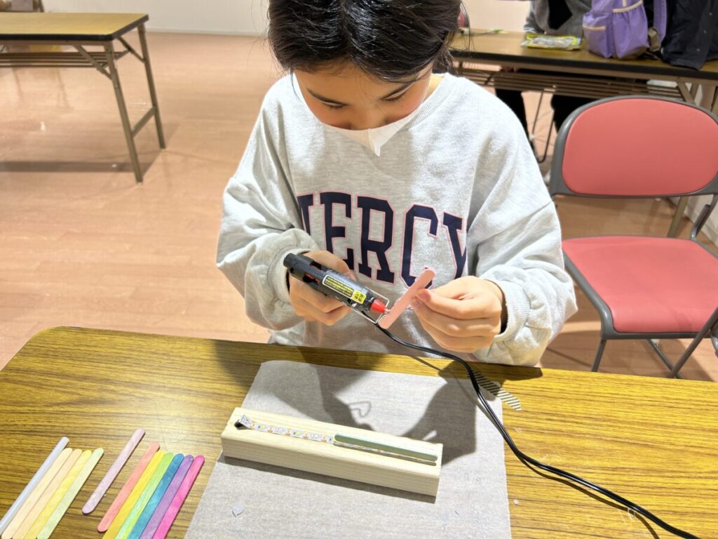 キッズテックエキスポの電子工作ワークショップで子どもがグルーガンを使って光るボードを制作する様子