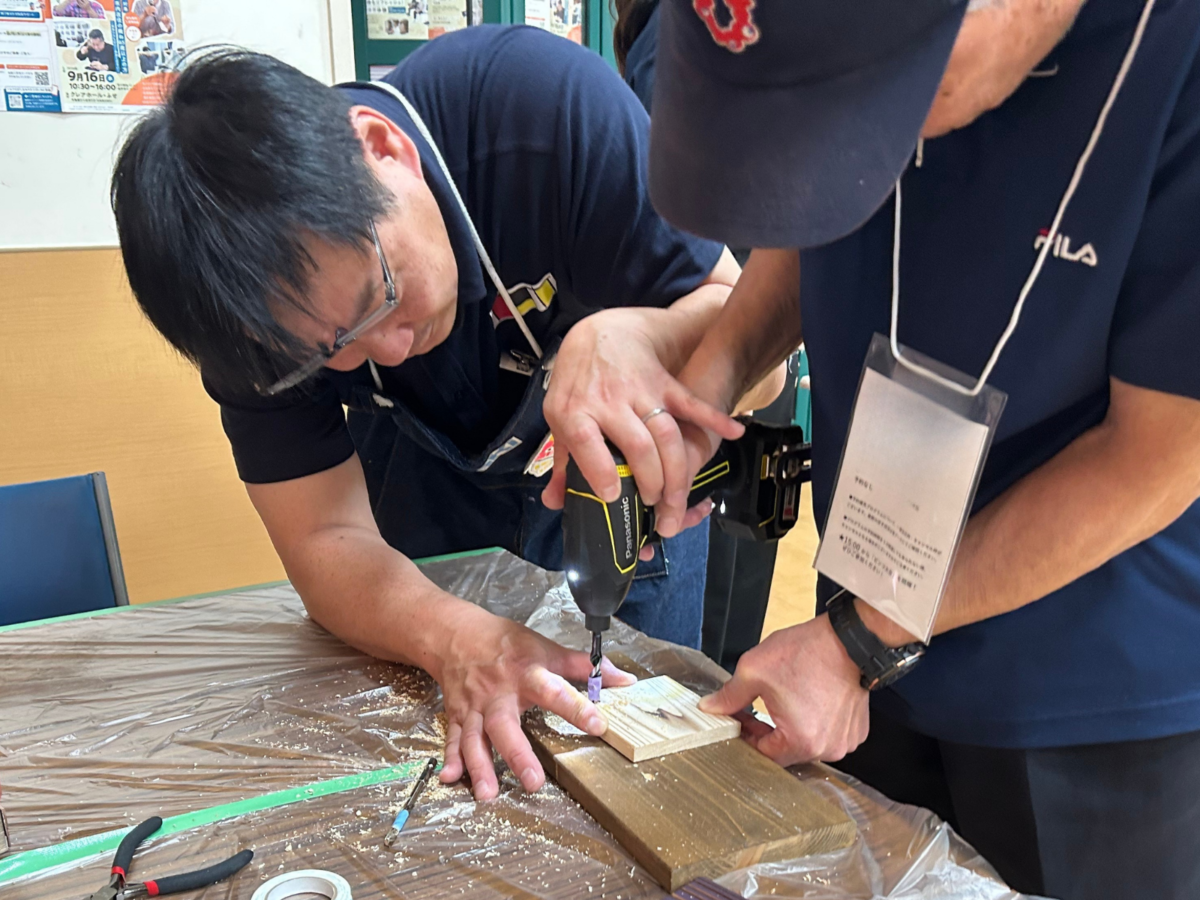 トルクフェスタのシニア向けDIYワークショップでDIYアドバイザーと電動ドライバーを使って木材に穴あけする様子